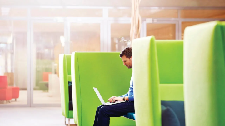 A man sits in a lime green chair and uses a laptop computer