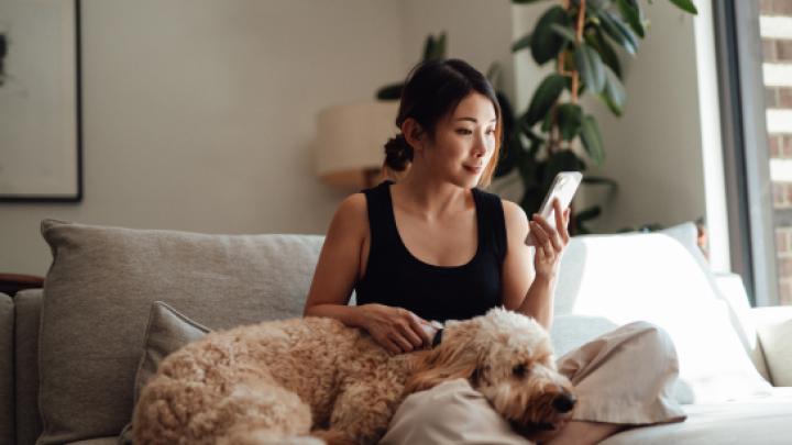 A woman sits with her dog and looks at her phone