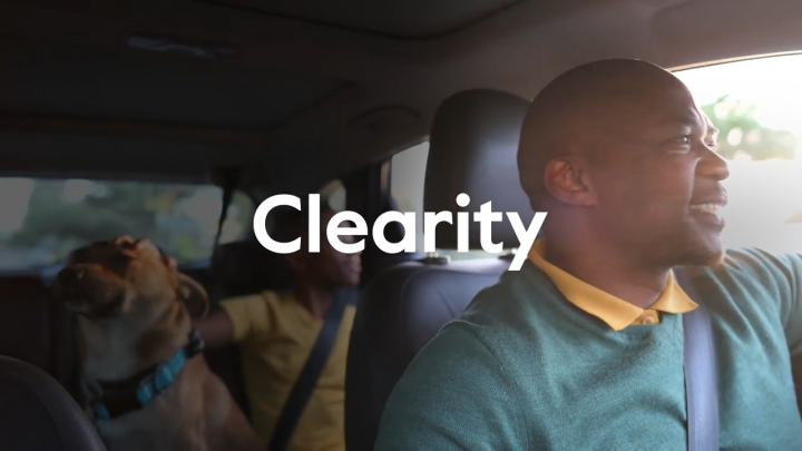 Man driving a car with dog in back seat, Clearity logo overlaid on image.