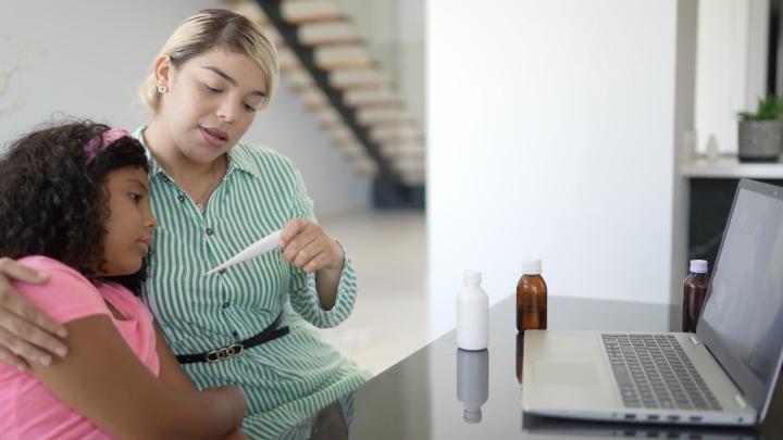 A caregiver takes her child's temperature during a virtual health visit