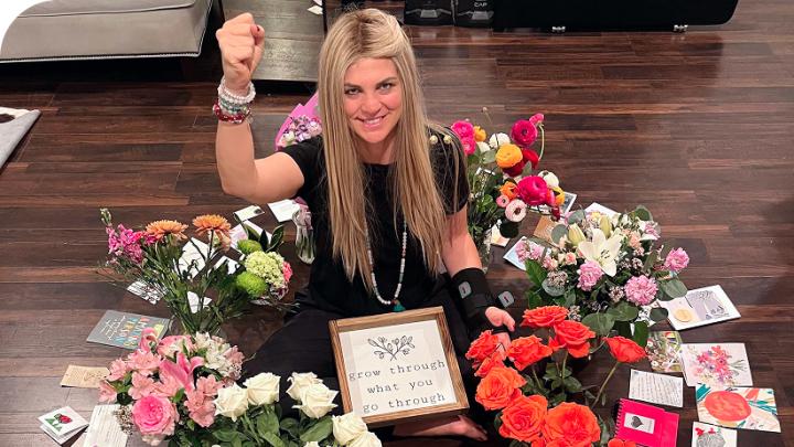A woman sits surrounded by flowers and cards sent by supporters