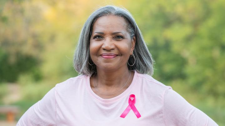 A smiling woman wears a pink shirt bearing the breast cancer awareness ribbon