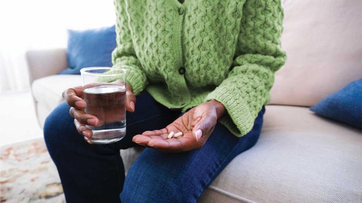 A person holds pills in one hand and a glass of water in the other