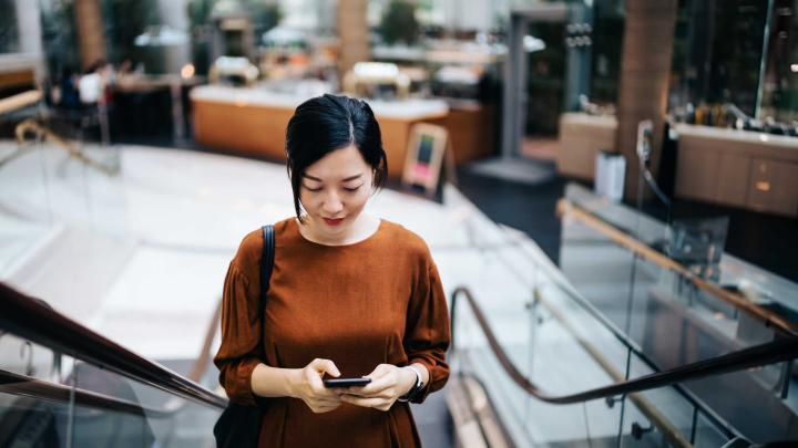 A woman uses a smartphone while riding an escalator