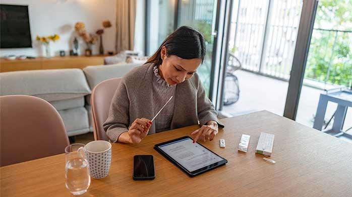 A woman sits at a table and reviews content on a tablet