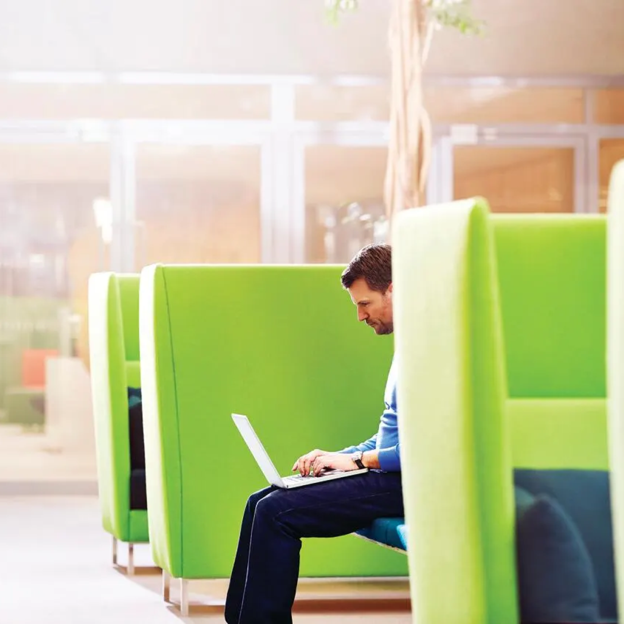 A man sits in a lime green chair and uses a laptop computer