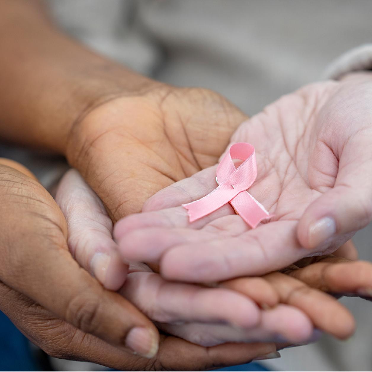 women stack their hands and hold a pink breast cancer support ribbon