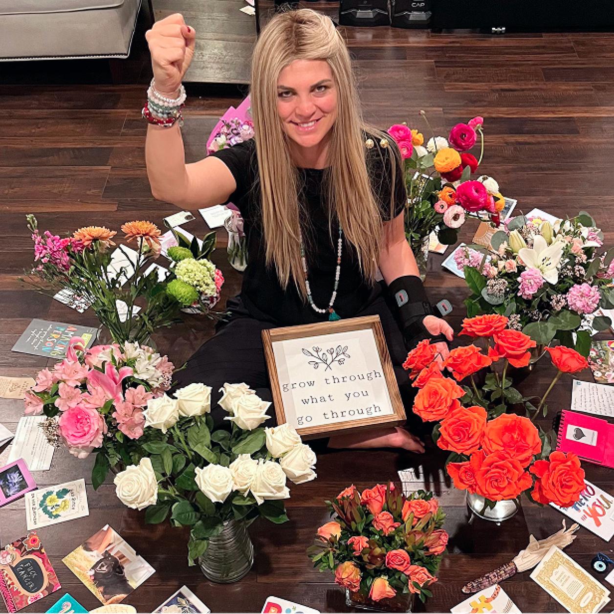 A woman sits surrounded by flowers and cards sent by supporters
