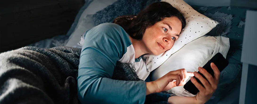 woman uses smartphone while laying in bed