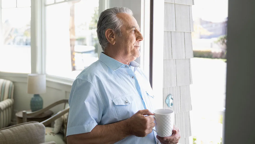 A man holds a mug and looks out a window