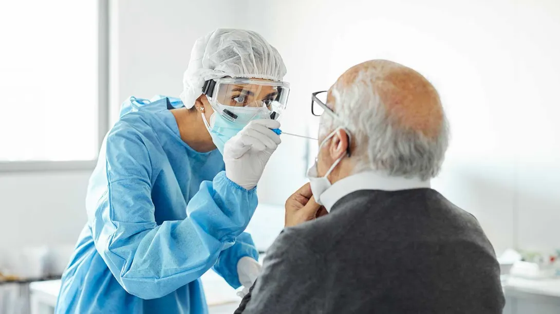 A medical professional wearing PPE swabs a man's throat