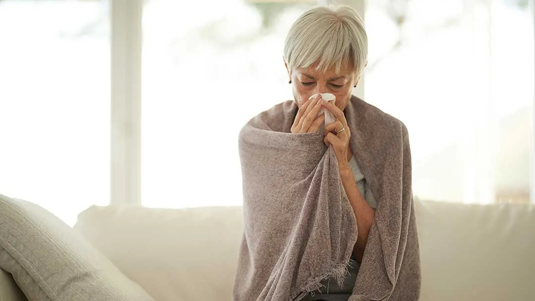 a woman wrapped in a blanket blows her nose