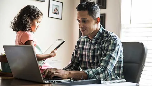 A man works on a computer while a little girl uses a tablet