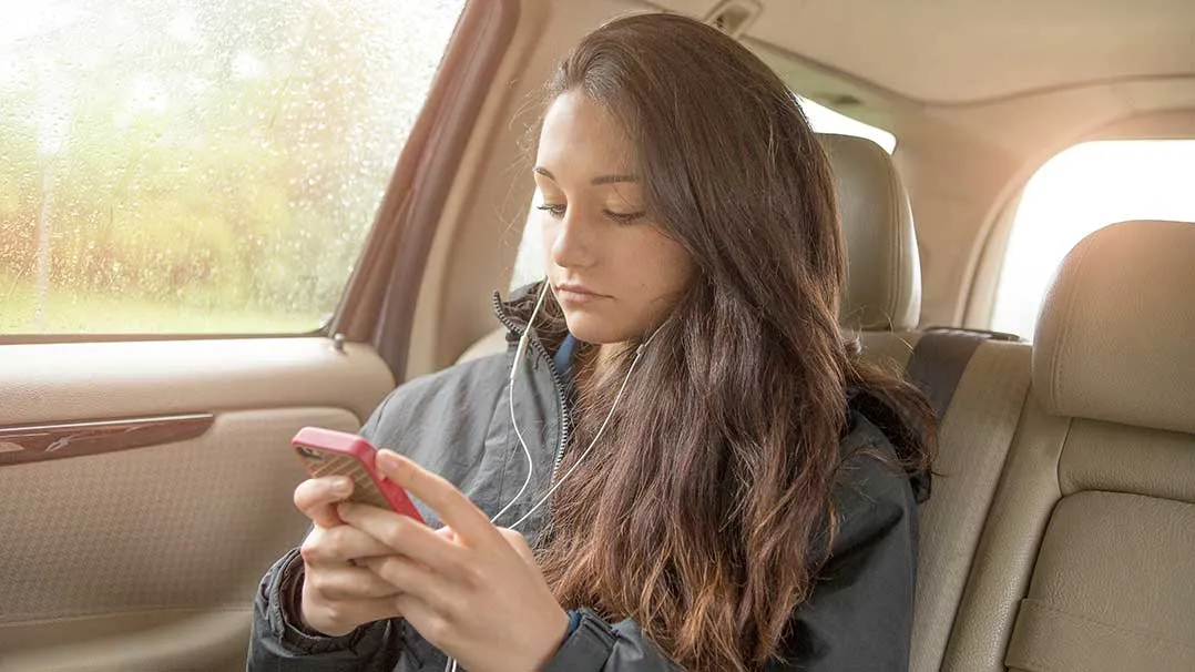 A woman sits in a car and uses a smartphone